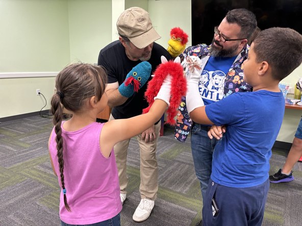 Children using handmade sock puppets with two instructors during a library ventriloquism workshop